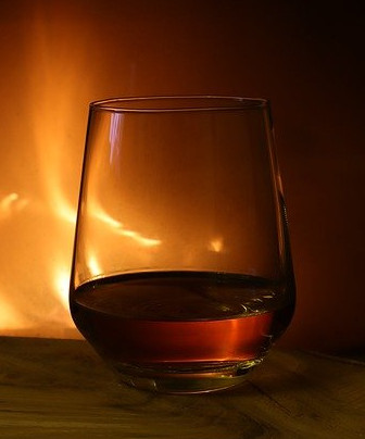 Glas mit Whisky vor Feuer