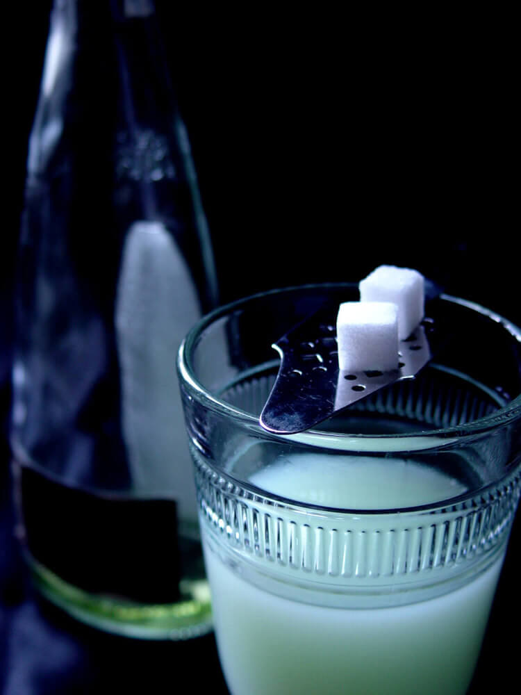 So trinkt man Absinth ein Glas mit Absinth und silbernem Loeffel mit zwei Zuckerwuerfel